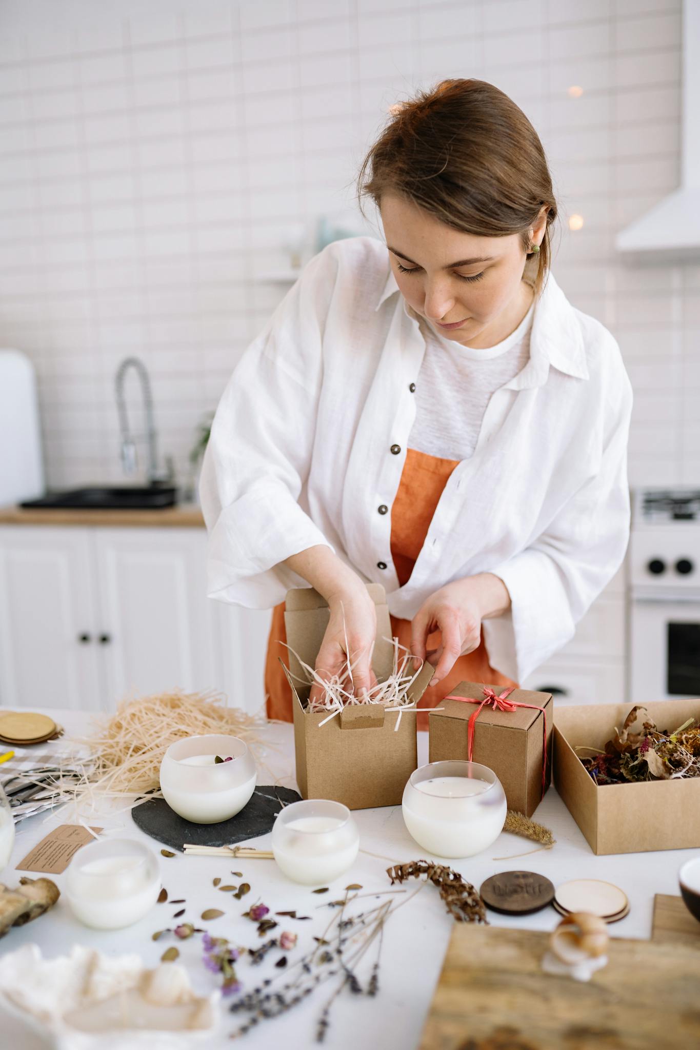 Woman carefully crafting and packing handmade candles in a cozy kitchen setting, emphasizing creativity and craft.